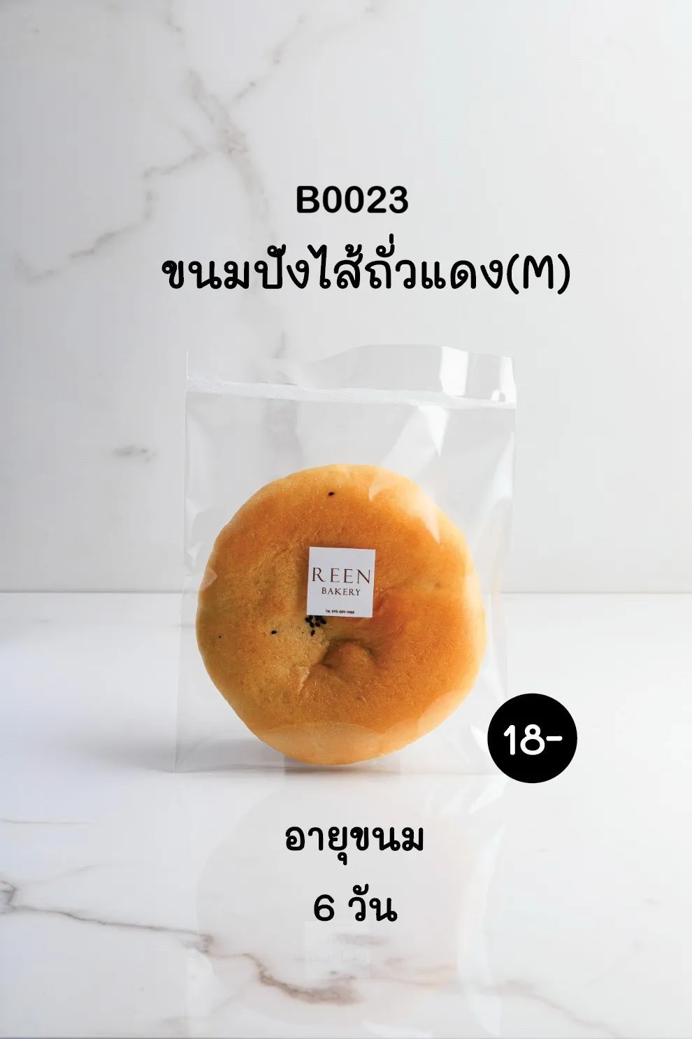 ขนมปังไส้ถั่วแดงทรงกลมขนาดกลาง บรรจุในถุงพลาสติกใส มีป้ายโลโก้ REEN BAKERY บนขนม วางอยู่บนพื้นผิวลายหินอ่อนสีขาว