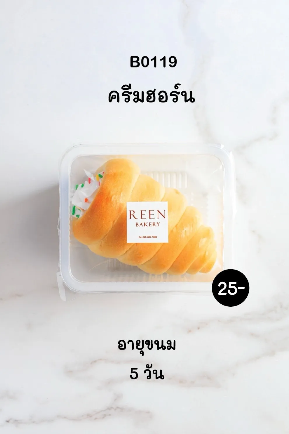 ขนมปังครีมฮอร์นหนึ่งชิ้นในกล่องพลาสติกใส ขนมปังสีทองเกลียวสวย ด้านในสอดไส้ครีมสีขาว โรยหน้าด้วยเกล็ดน้ำตาลหลากสี มีฉลาก REEN BAKERY ติดอยู่